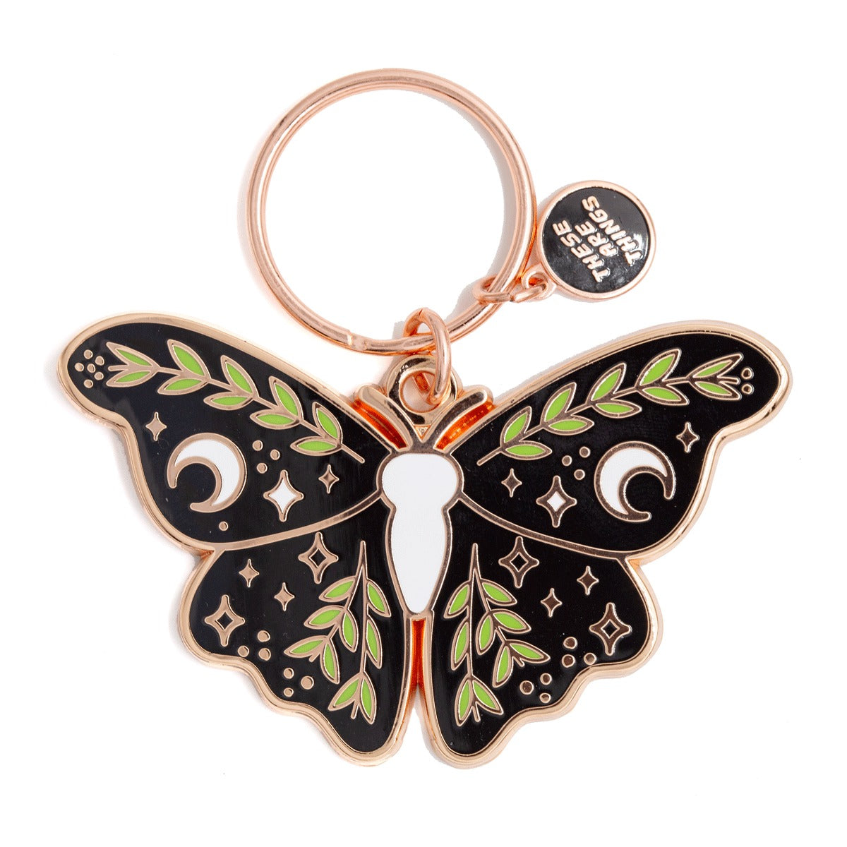 Porte-clef et breloque en forme de papillon de nuit. Le porte-clef est en émail de couleur or. Les ailes noires du papillon sont décorées de feuilles vertes, de lunes et d’étoiles blanches. Il y a aussi de petites étoiles or sur toutes les ailes. Il y a une toute petite breloque sur laquelle est inscrit le nom de la marque qui est There are things. L’arrière-plan est un fond blanc. 