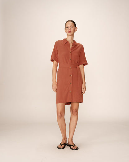 Robe chemise de la marque Grace & Mila, modèle Paquita, en coloris terracotta. Cette robe fluide à manches courtes présente une coupe droite élégante, soulignée par une ceinture assortie qui permet d'ajuster la silhouette. Son col chemise et sa patte de boutonnage ajoutent une touche classique et raffinée. Confectionnée dans une matière légère et confortable, elle est idéale pour la saison estivale. Portée avec des sandales ou des baskets, elle s'adapte à toutes les occasions pour un style décontracté.