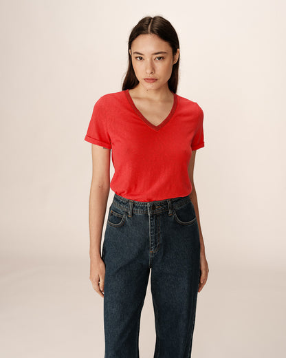 L’image montre une jeune femme portant un T-shirt rouge à col en V, rentré dans un jean taille haute en denim foncé.