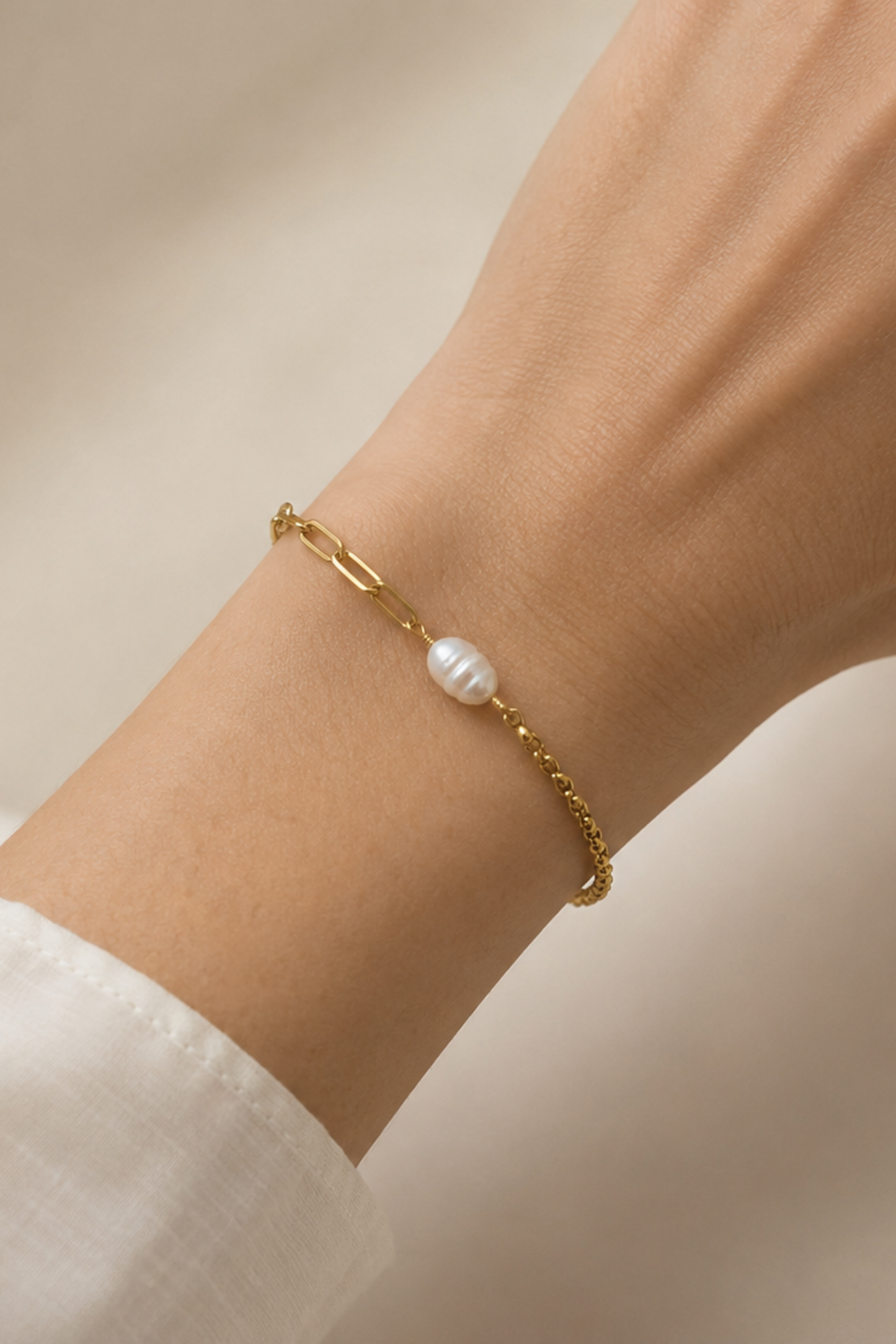 Bracelet Perla Or porté au poignet avec chaîne dorée asymétrique et perle d’eau douce centrale.