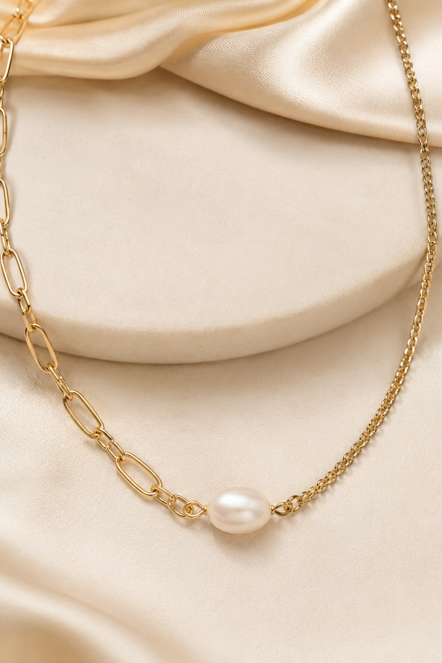 Collier Perla Or doré avec chaîne asymétrique et perle d’eau douce sur fond satiné élégant.