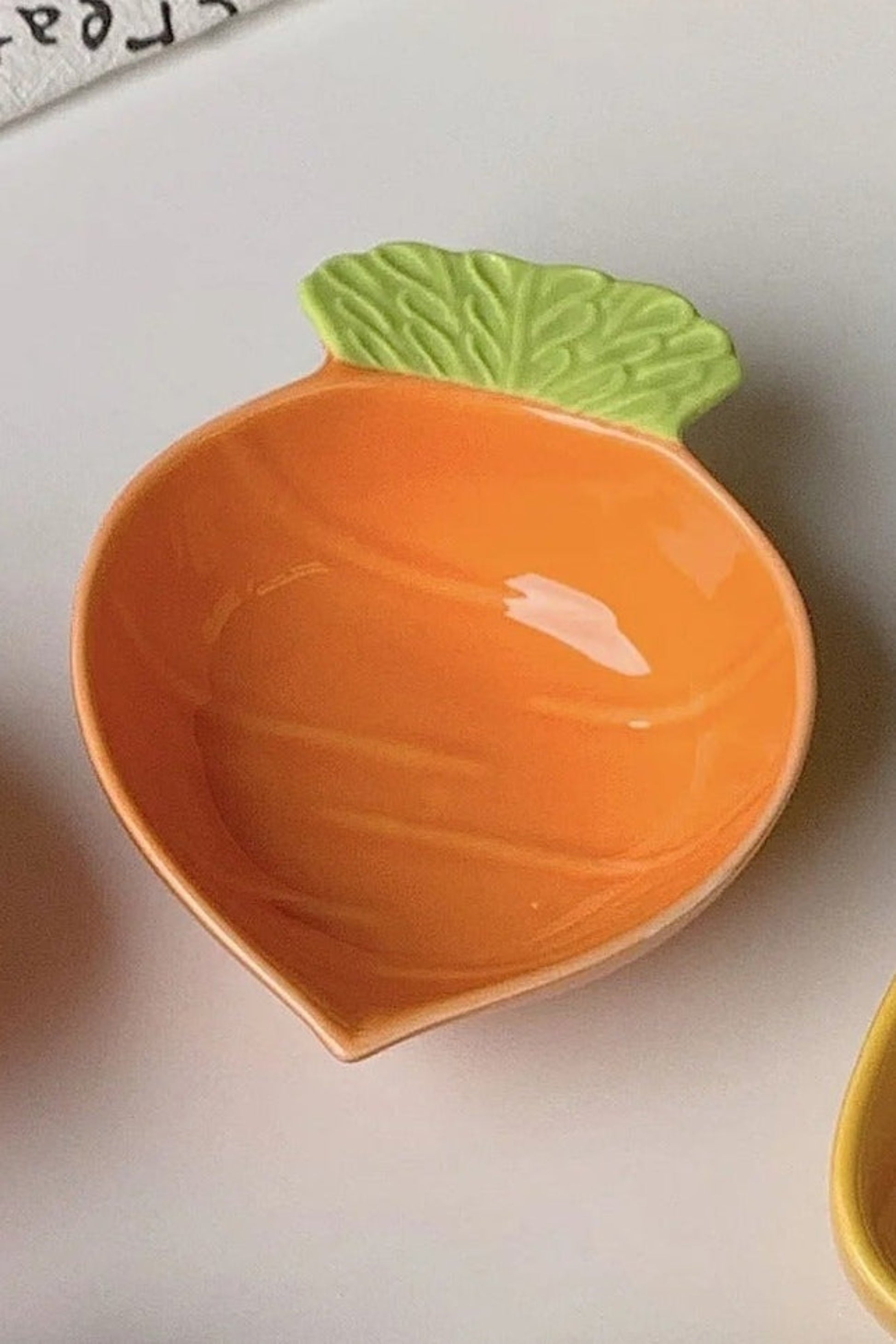 Petit plat en céramique orange en forme de carotte, avec feuille verte