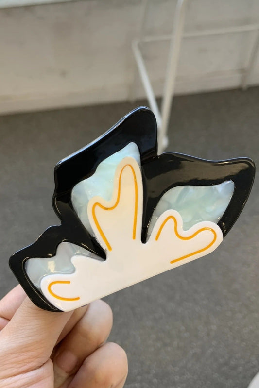 Pince à cheveux Papillon en acétate noir, blanc nacré et détail orange – accessoire chic et original.