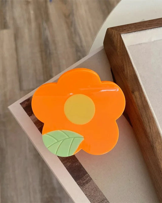 Pince à cheveux en acétate 6 x 7 cm en forme de fleur orange avec centre jaune et feuille verte, vue de dessus
