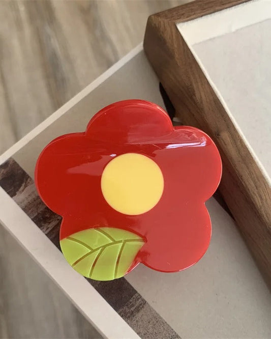 Pince à cheveux en acétate 6 x 7 cm en forme de fleur rouge avec centre jaune et feuille verte, vue de dessus
