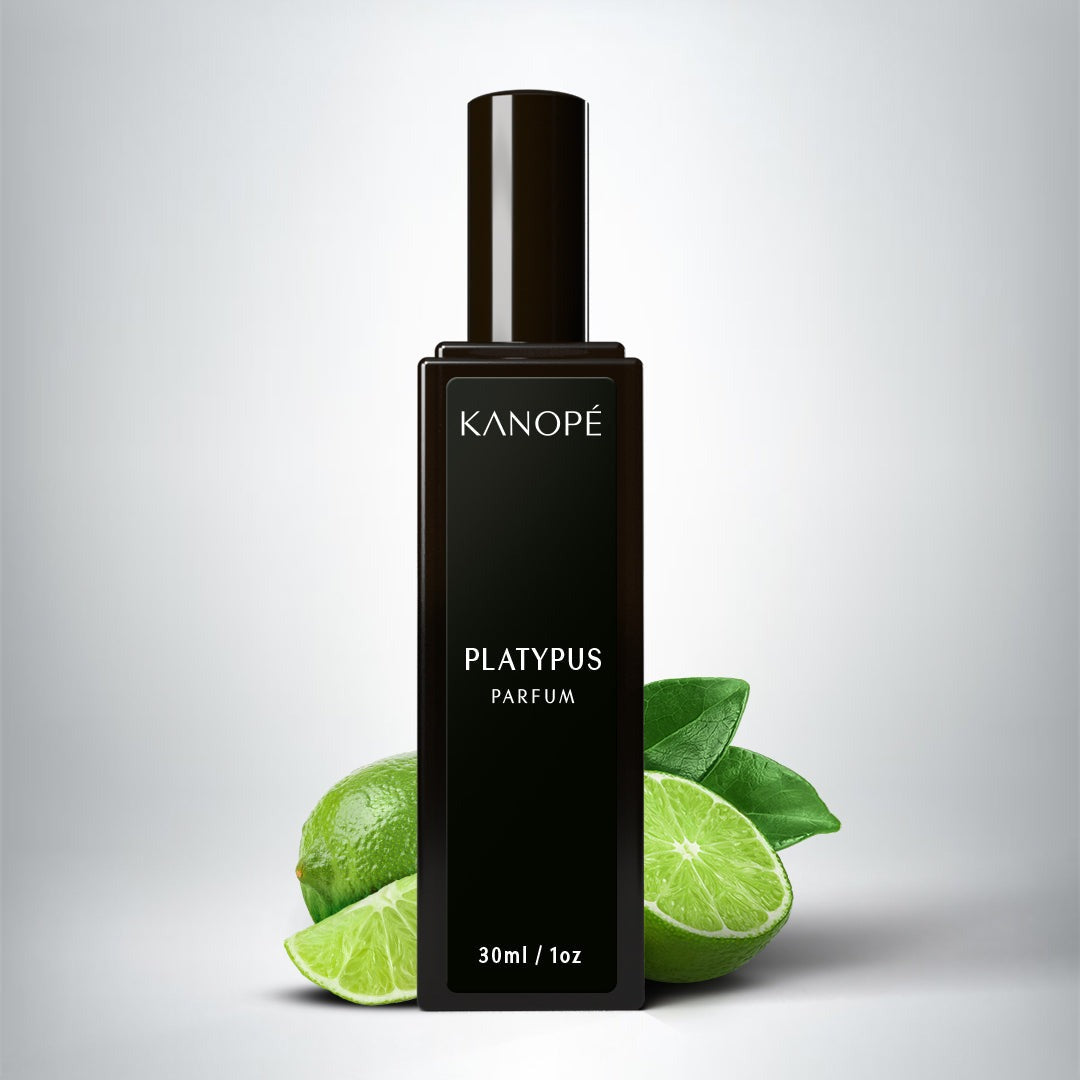 Le parfum est présenté dans une petite bouteilles rectangle en verre noir. Une étiquette noire est collé sur le long de la bouteille. On peut lire Platypus et en en-dessous eau de parfum. Derrière la bouteille, on peut voir des citrons verts entiers et découpés. L'arrière plan est un fond gris.