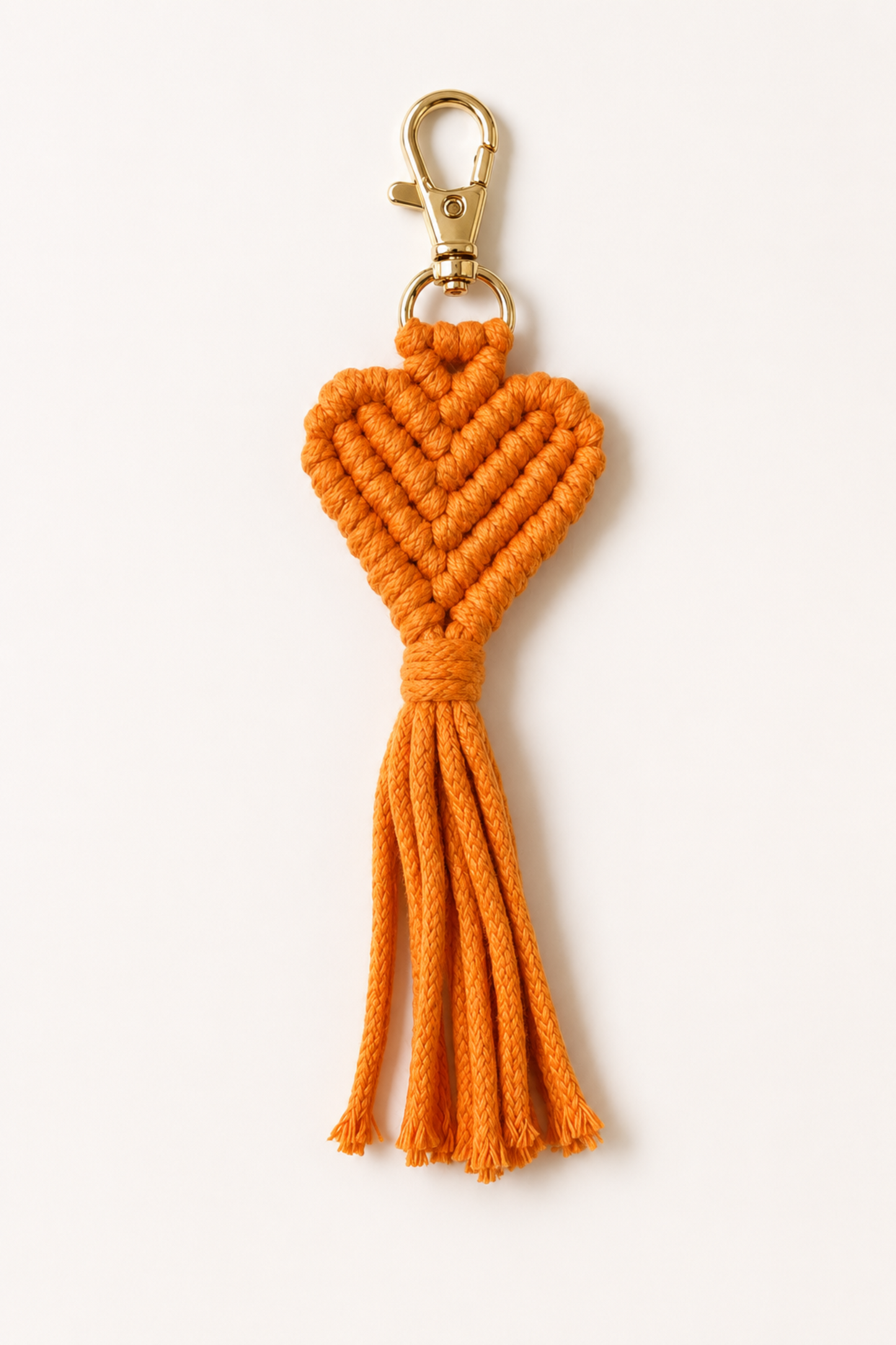Porte-clé cœur en macramé orange avec frange longue et mousqueton doré.