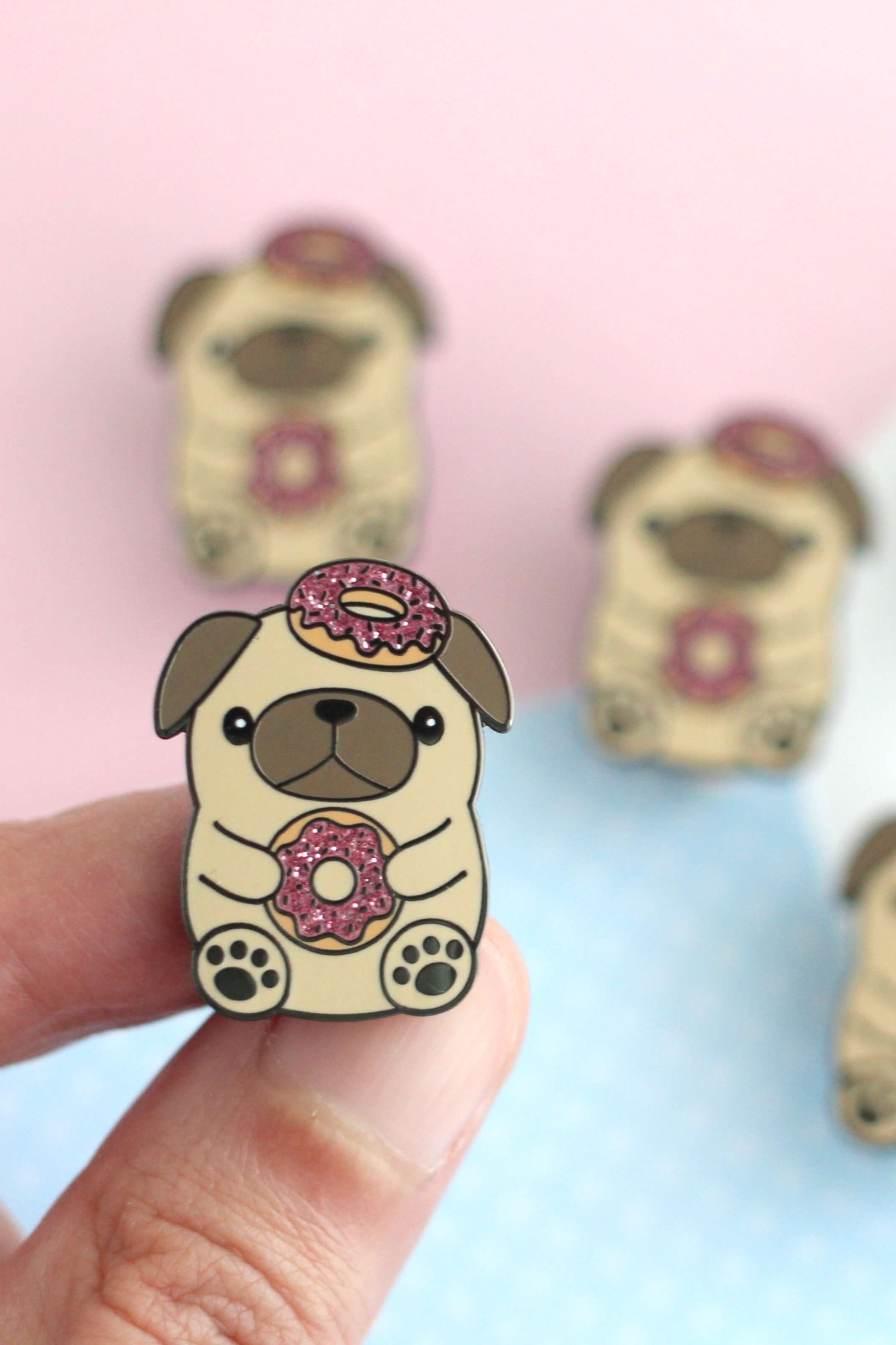 Épinglette pug donut tenue entre les doigts – détail paillettes roses