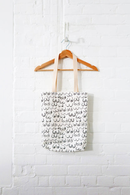 Sac fourre-tout Seins suspendu contre un mur blanc – motif artistique noir sur fond crème.