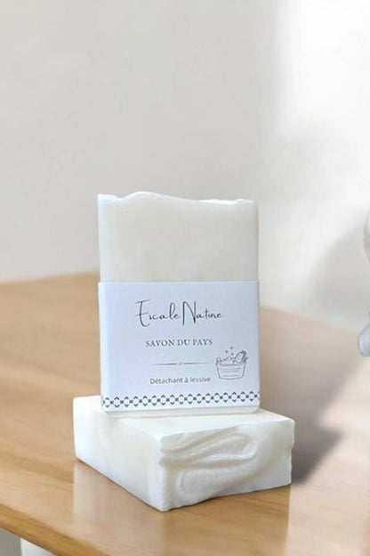 Savon du pays détachant blanc placé sur une table avec linge plié + nettoyant naturel pour taches
