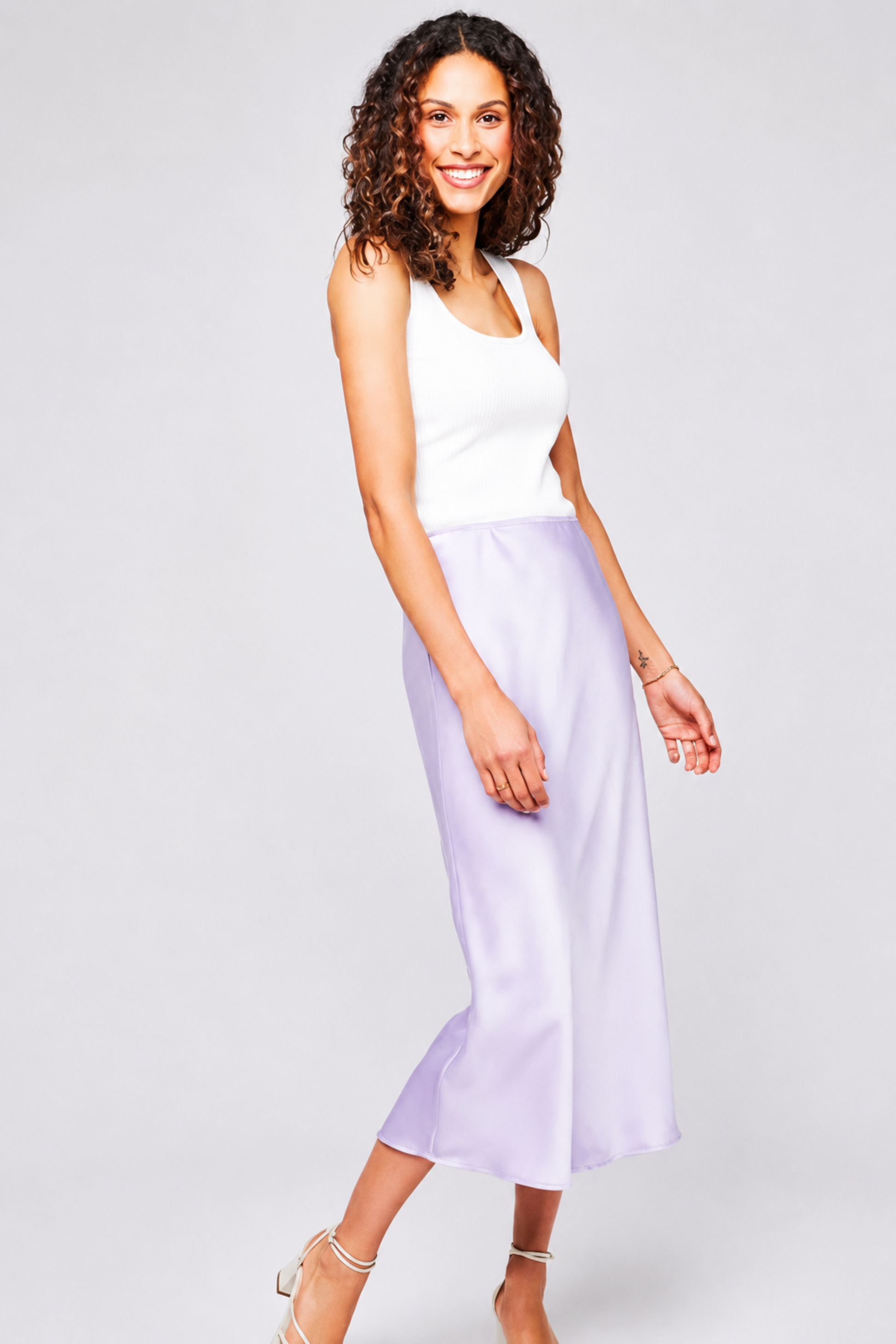 Jupe Selena mauve portée avec une camisole blanche, coupe midi fluide et fini satiné brillant.