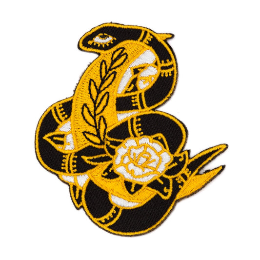 Patch en forme de serpent noir enlaçant un croissant de lune jaune et une fleur blanche. L’arrière-plan est un fond blanc. 