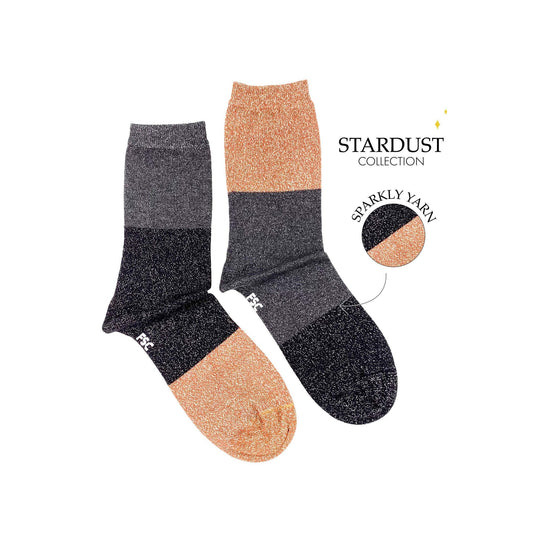 Paire de chaussettes dépareillées sur fond blanc. Les chaussettes sont découpées en trois grosses bandes. Une chaussette a une première bande grise puis une noire et une beige. L’autre chaussette à une première bande beige puis une grise et une noir. Ce sont des chaussettes à paillettes.  