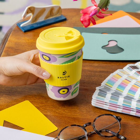 Tasse réutilisable Sérénade avec fleurs lilas – tenue en main, sur bureau coloré