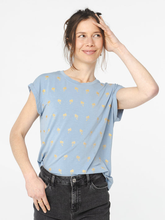 Femme portant un t-shirt bleu pastel à motifs palmiers or avec coupe décontractée